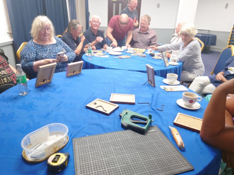 A group of people sitting at two round tables making picture frames for their own photos | VOS