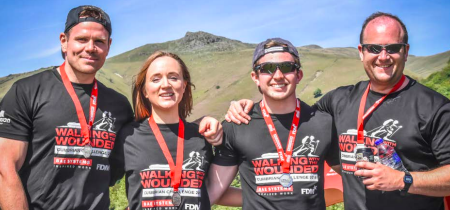 Four people standing in front of a mountain, each with medals around their neck and t-shirts with the Walking With The Wounded charity logo on them | VOS