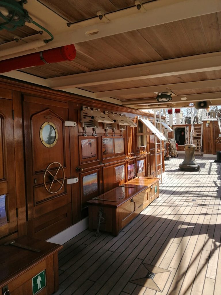 A view along one of the lower decks of RNOV Shabab Oman II. There is a lot of varnished wood decoration. | VOS