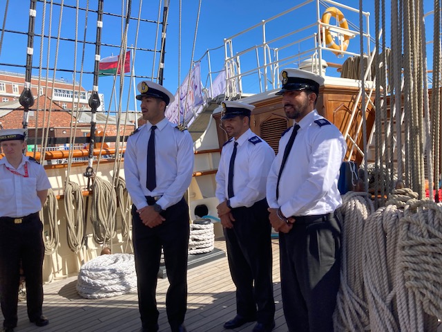 Four crew members of RNOV Shabab Oman II aboard the ship. They are wearing black trousers, white shirts, black ties and white and black Navy caps. | VOS