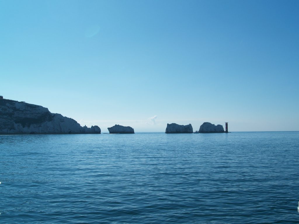 A view across the sea of the Needles on the Isle of Wight. The sea is calm and a deep blue, and the sky is bright blue with no clouds. | VOS