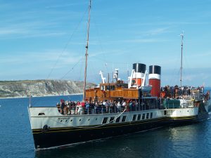 Paddle Steamer Waverley on the sea at Swanage, with cliffs in the background. There are lots of people standing aboard her. | VOS