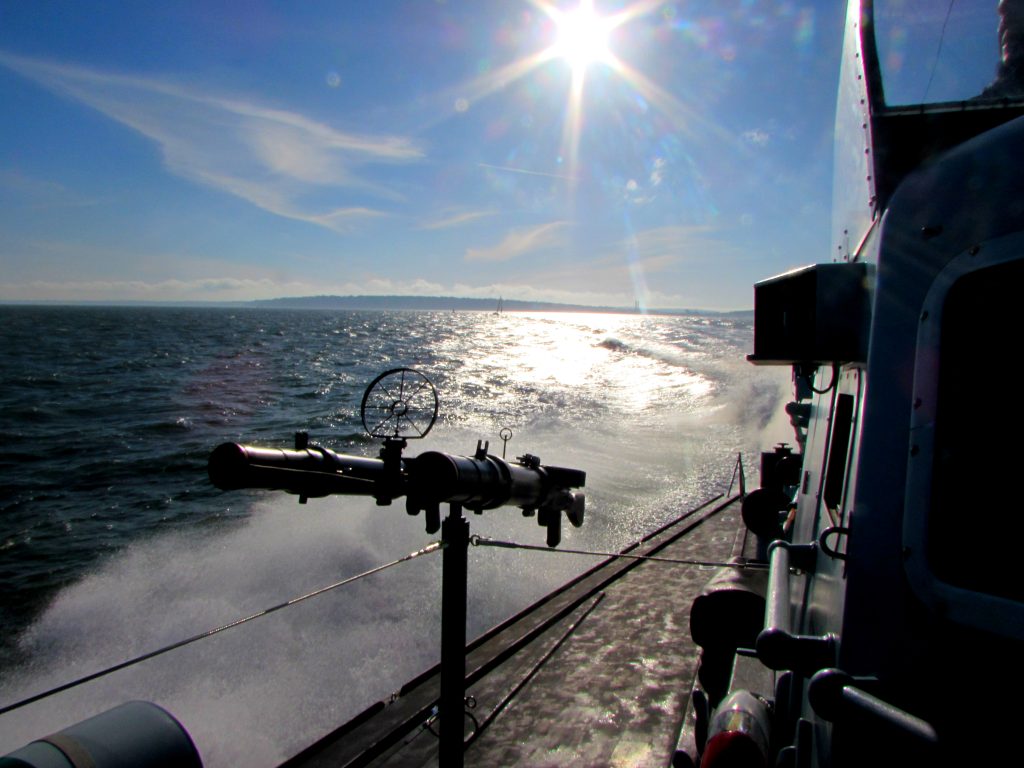 A photo of one of the guns aboard Motor Gun Boat 81, which is a small Royal Navy vessel from World War II. In the background the sun is shining brightly on the sea and the sky is blue. | VOS