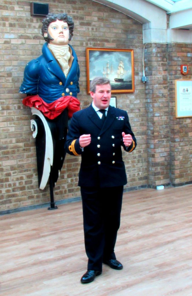 A Royal Navy officer standing in front of a ship figurehead which is mounted on the wall inside HMS President in London. | VOS