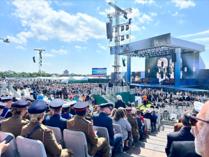 Crowd of soldiers and civilians watching the huge D-Day 80 ceremony on a large stage and video screen in Southsea UK.