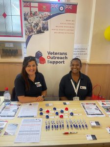Two women in blue golf shirts sitting behind a help desk at a VOS Veterans Drop-In Day in the ballroom at the Royal Maritime Hotel, Portsmouth